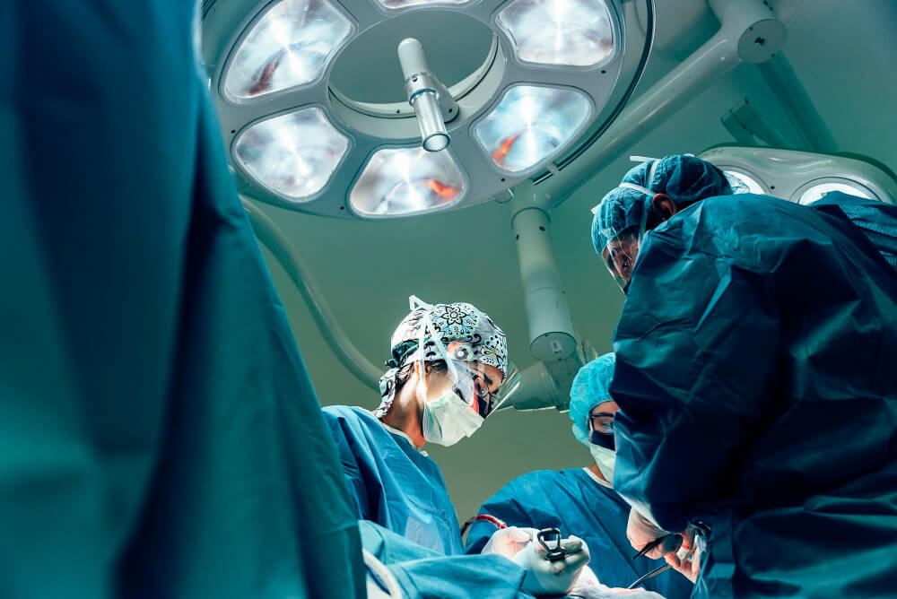 imagem de cima para baixo em mesa de cirurgia, mostrando luzes médicos ao entorno